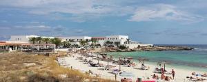 a beach with a group of people sitting on the sand at Hotel Roca Bella in Es Pujols