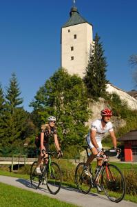 Dwóch mężczyzn jeżdżących rowerami po drodze przed wieżą w obiekcie Hotel Kraftquelle Schlossblick w mieście Angerberg