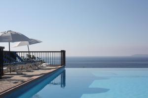 a pool with chairs and an umbrella and the ocean at Résidence Goélia Le Domaine de la Pinède in Le Lavandou