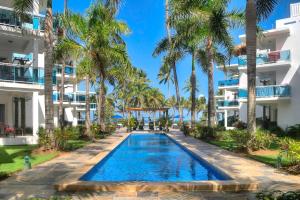 a swimming pool in front of a building with palm trees at Palmeraie Terrenas Beach Apartment in Las Terrenas
