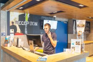 a man talking on a cell phone at a counter at ibis budget Rennes Rte Lorient in Rennes