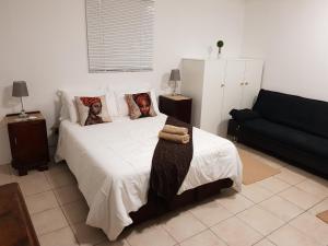 a bedroom with a white bed and a black couch at African Dwarf Kingfisher Guesthouse in Eshowe