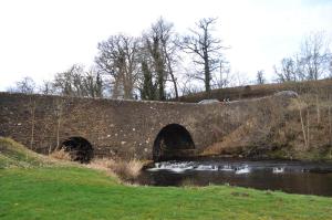 een stenen brug over een rivier in een veld bij Bridgehill Cottage Bed & Breakfast in Crieff