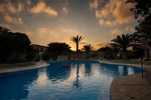 a large swimming pool with a sunset in the background at Hotel Luci Del Faro in Calasetta