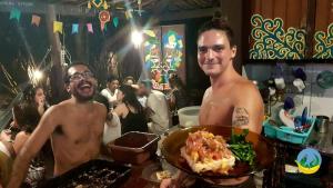 two men holding a plate of food in a restaurant at Lagarto Na Banana Hostel in Pipa
