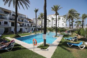 马尼尔瓦Apartamento 409 Marina Real Puerto de la Duquesa playa的度假村内带椅子和棕榈树的游泳池