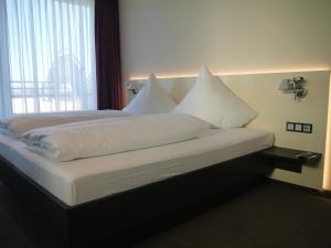 Bett mit weißer Bettwäsche und Kissen in einem Zimmer in der Unterkunft Hotel am Berg Esslingen in Esslingen