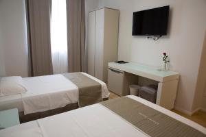 a room with two beds and a desk and a television at Boutique Hotel Enia in Prato