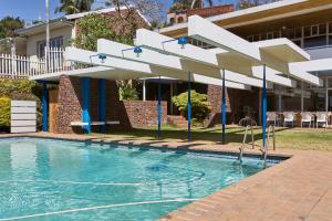 a swimming pool in front of a house with a white umbrella at House Sandrock Muckleneuk Selfcatering apartment in Pretoria