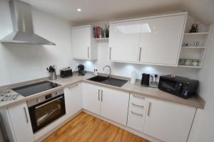 cocina con armarios blancos, fregadero y microondas en Alberts Dairy Cottage en East Cowes