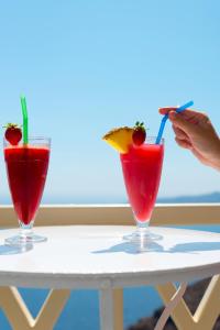 two cocktails on a table with a person eating a piece of food at Pearl on the Cliff Hotel & Suites by Pearl Hotel Collection in Imerovigli