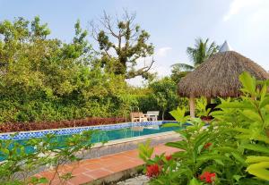 a swimming pool in a garden with a grass umbrella at Riverside Park Eco Resort in Vĩnh Long
