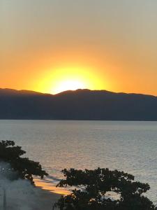 um pôr-do-sol sobre a água com árvores em primeiro plano em Cobertura frente ao mar em Florianópolis