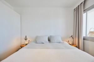 a white bedroom with a large bed and a window at Sunny Beachfront Escape in Castelldefels