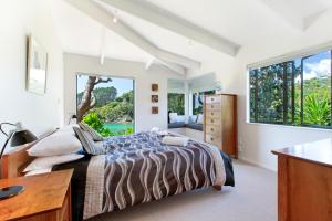 a bedroom with a bed and a desk and windows at Beachfront Enclosure Bay - Waiheke Unlimited in Oneroa