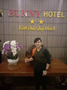 a man standing next to a table with a vase of flowers at Sunny Hotel in Phan Rang