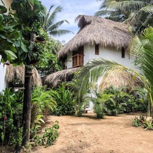 a white house with a thatched roof and palm trees at Hotel Descalzo in Zipolite