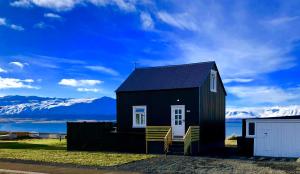 a black tiny house with snow covered mountains in the background at Vellir Grenivík Home with a View in Grenivík