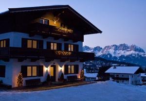 un bâtiment dans la neige avec des montagnes en arrière-plan dans l'établissement Pension Feiersinger, à Kitzbühel