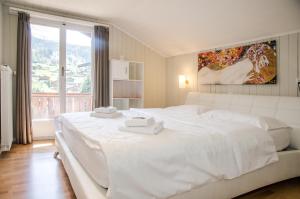 a white bedroom with a large white bed and a window at Chalet D in Grindelwald