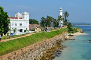a white building next to a river with a lighthouse at Old Dutch House in Galle
