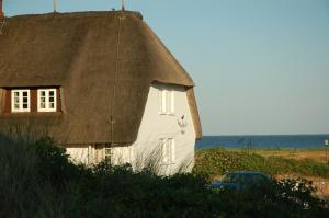 a white house with a thatched roof next to the ocean at Hotel Watthof in Rantum