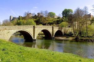 eine Steinbrücke über einen Fluss mit einem Schloss im Hintergrund in der Unterkunft Hampton Wafre Cottage in Docklow