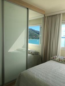1 dormitorio con espejo, cama y ventana en Apartamento frente ao mar, en Balneário Camboriú
