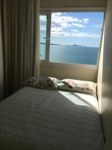 a bed with two pillows in front of a window at Apartamento frente ao mar in Balneário Camboriú