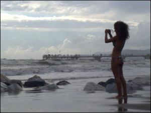 a woman standing on the beach taking a picture of the ocean at Hotel Naviglio in Marina di Pietrasanta