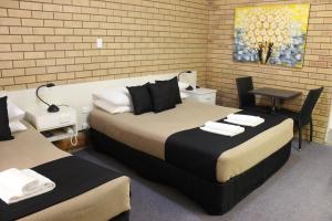 a room with two beds and a table and a desk at Golden Harvest Motor Inn Moree in Moree