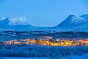 a building in a field with mountains in the background at STF Abisko Turiststation in Abisko