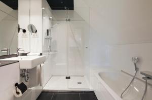 een witte badkamer met een douche, een wastafel en een bad bij Schulhaus Hotel in Schwelm