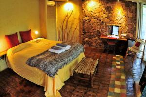 1 dormitorio con 1 cama grande y pared de piedra en Cuatrovientos Hostería en San Javier