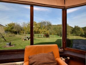 uma cadeira laranja em frente a uma janela com vista para um campo em Rustic house with sunroom em Petit-Thier