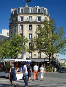 um grupo de pessoas andando em torno de um mercado em frente a um edifício em Hôtel Odessa Montparnasse em Paris