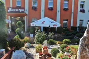 einen Garten mit einem Sonnenschirm und Pflanzen vor einem Gebäude in der Unterkunft Hotel Bursztyn in Kalisz
