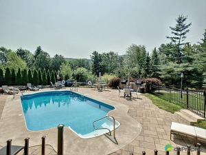 - une grande piscine dans une cour avec des chaises et des arbres dans l'établissement Condo Le Champlain - 105, à Bromont