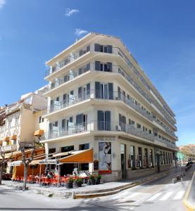 un edificio blanco alto en una calle de la ciudad con mesas en Hotel Subur, en Sitges