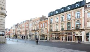 a man riding a bike down a street with buildings at Theater Hotel Leuven Centrum in Leuven