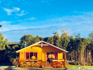 a small yellow house with red windows and a porch at Cabañas Los Fabianes in Castro