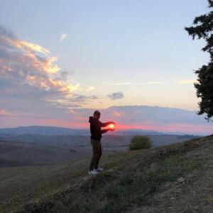 un homme debout sur une colline et regardant le coucher du soleil dans l'établissement Agriturismo Il Colombaiolo, à Pienza