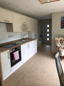 una cucina con armadi bianchi, lavandino e sedia di Coastal Retreat a Lowestoft