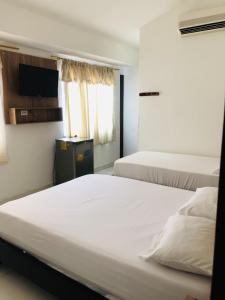 two beds in a room with white sheets at Hotel Center Plaza Plus in Cúcuta
