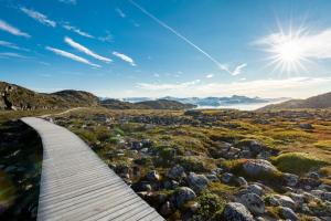 a boardwalk in a field with rocks and the sun at Hotel Icefiord in Ilulissat