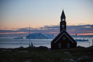a church sitting on top of a field with the ocean at Hotel Icefiord in Ilulissat