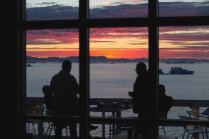 a group of people sitting in a window watching the sunset at Hotel Icefiord in Ilulissat
