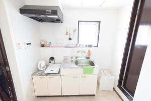 Elle comprend une petite cuisine blanche avec un évier et une fenêtre. dans l'établissement Cocostay Jarudan ココステイ ジャルダン, à Hiroshima