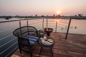 a table and chairs on a deck with a view of the water at The Namushasha River Villa in Kongola