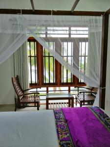 a bedroom with a bed and two chairs and windows at Hikka Lagoon in Hikkaduwa
